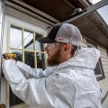 Weatherization technician standing outside installing weather stripping for a door.
