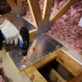 A technician is using a drill to fasten rigid backer material to a framing above a dropped soffit.