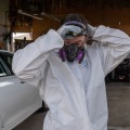 A weatherization worker wearing a white protective coverall and respirator positions a headlamp. 
