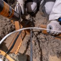 A weatherization installer dispenses an orange colored foam sealant to seal a gap from a partially insulated attic.