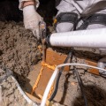 A weatherization installer dispenses an orange colored foam sealant to seal a gap from a partially insulated attic.