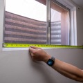 A weatherization installer measures the rough opening of a basement window using a tape measure.