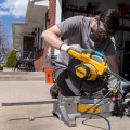A weatherization installer wearing safety goggles uses a miter saw to cut a metal storm window frame.