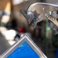 Close up view of a mitered metal frame of a plexiglass window with the hand of a worker holding a crimping tool in the background. 