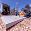 A worker kneeing on a sheet of rigid foam insulation while outside takes a measurement .