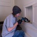 A worker holding a caulk gun applies sealant into a crack around an access opening.