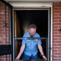 A person positioning an adjustable frame of a blower door system into a door opening.