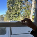 A hand turning a white locking mechanism of a window. 